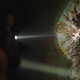 Tess shines a flashlight on an infected person who's been totally fused to the wall by fungal growth in a scene from HBO's The Last of Us.